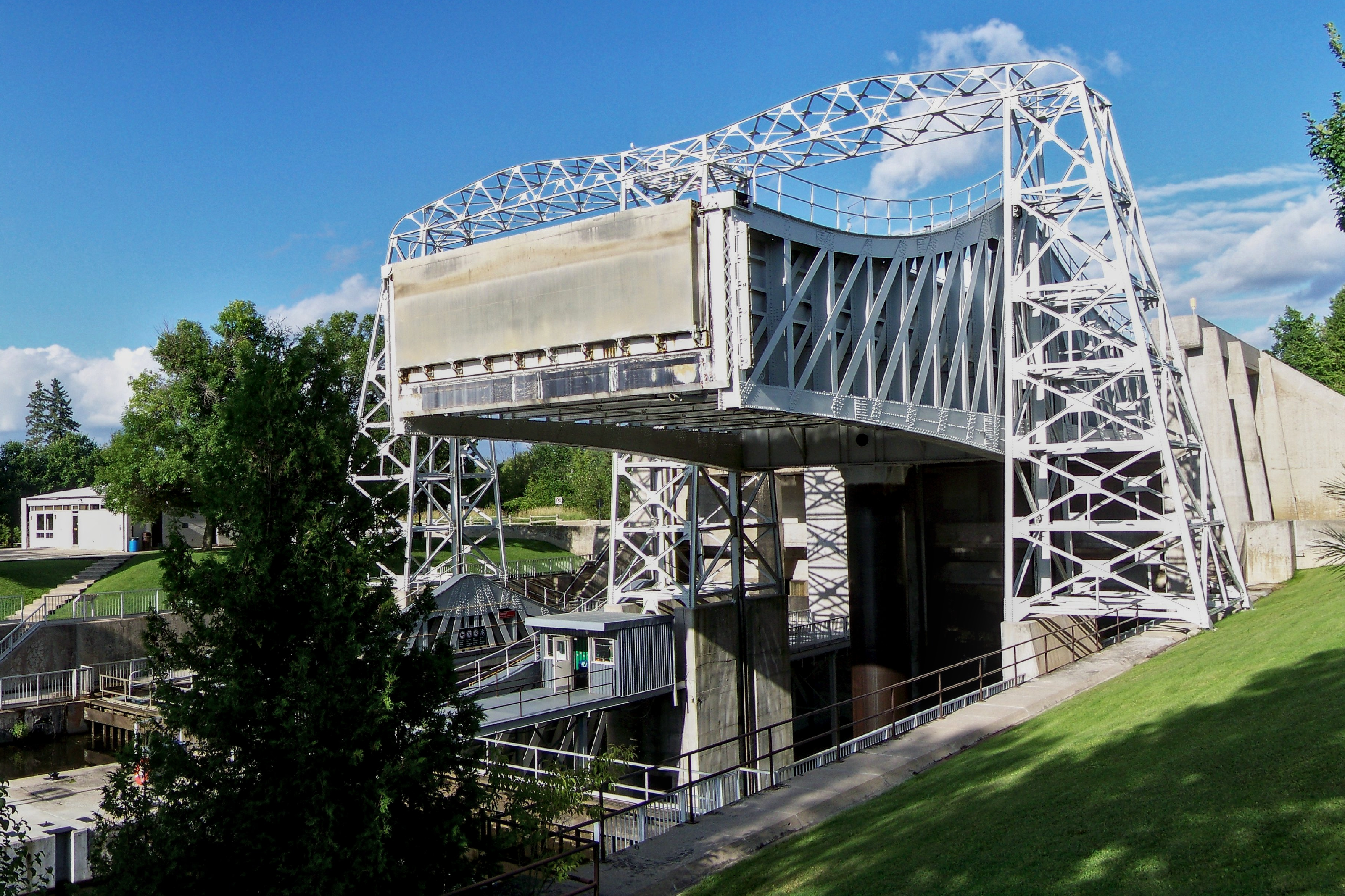 Exterior view of large, white-painted steel structure straddling a canal with one boat lift chamber in up position. 